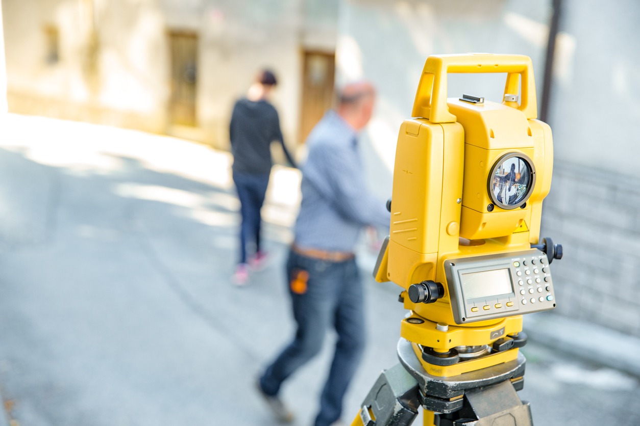 Theodolite With Surveyors in Background - Stock Photo