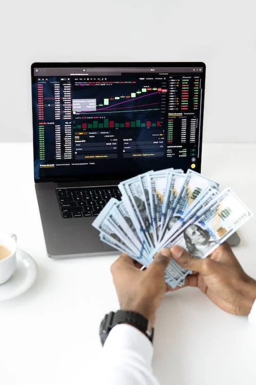 A person holding money in front of a laptop with graphs